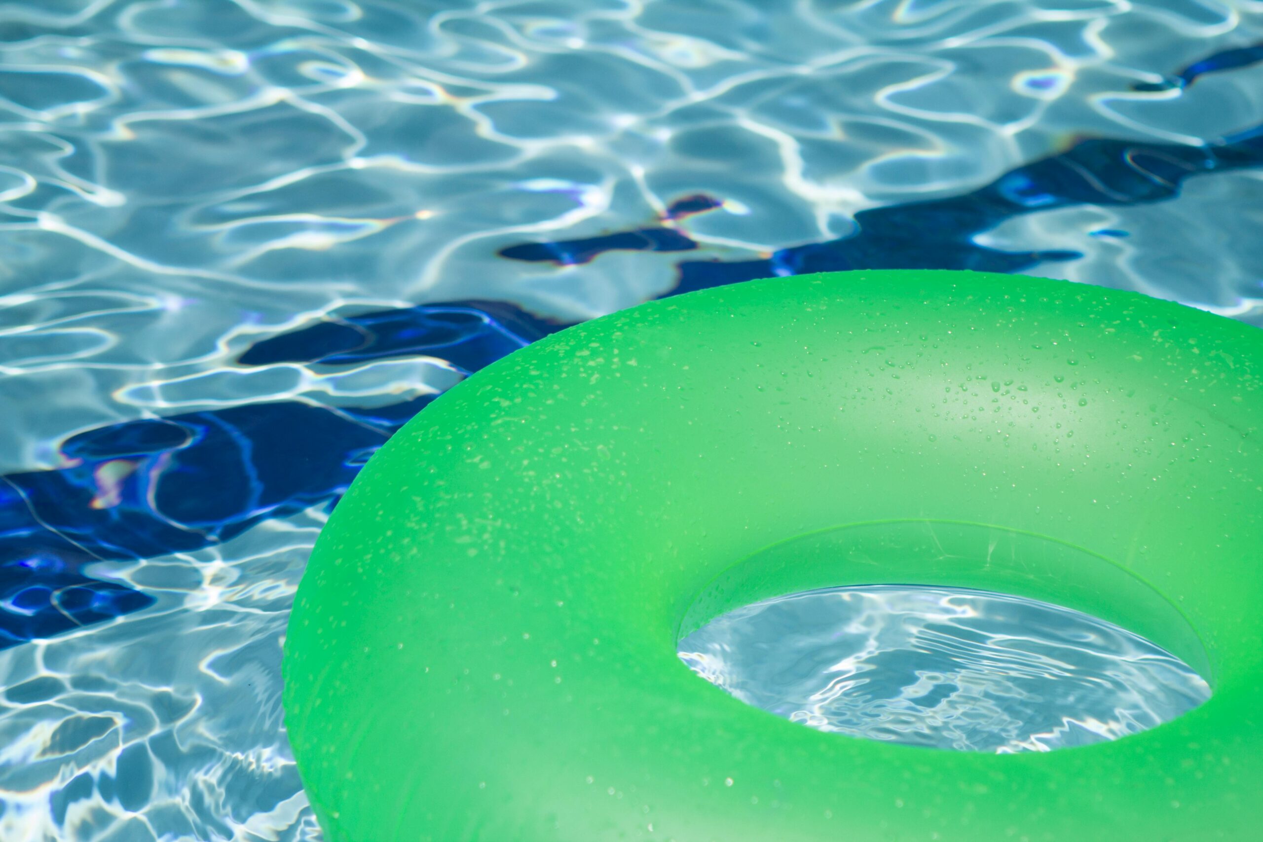 Luxurious in-ground swimming pool surrounded by stone patio and lush landscaping on a sunny day.
